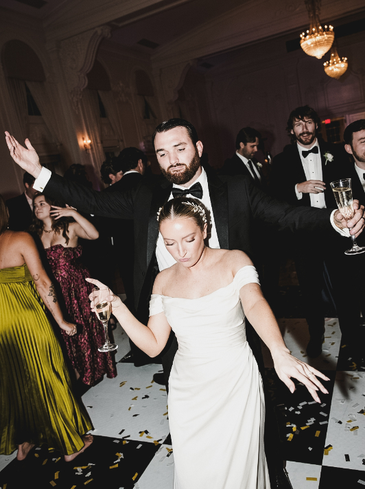 A bride and groom dancing on a checkered floor, each holding a glass of champagne.
