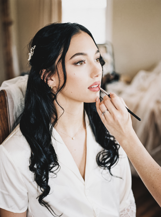 A makeup artist uses a brush to apply lipstick to a bride.